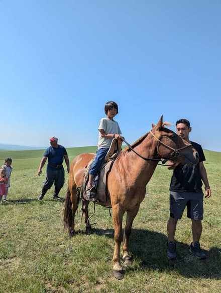 モンゴルの草原で馬に乗る息子